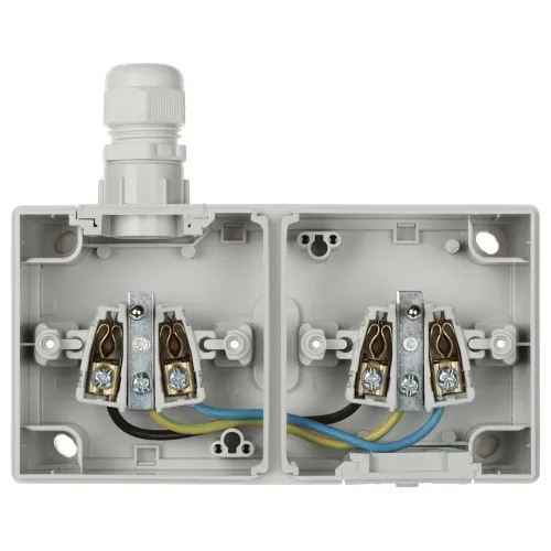 Zdjęcie przedstawia otwartą, dwukomorową puszkę elektryczną z widocznymi zaciskami i przewodami w kolorach niebieskim, żółto-zielonym i brązowym. Na górze znajduje się biały dławik kablowy.