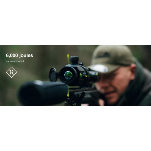 Osoba w czapce celuje z karabinu wyposażonego w celownik termowizyjny w leśnym otoczeniu. Na zdjęciu widoczny jest napis "6,000 joules maximum recoil" oraz logo.