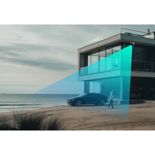 Nowoczesny dom przy plaży z dużymi szklanymi oknami, przed którym stoi samochód i przechadza się osoba. Na budynku zamontowana jest kamera IP, której zasięg monitoringu jest zaznaczony niebieskim światłem.