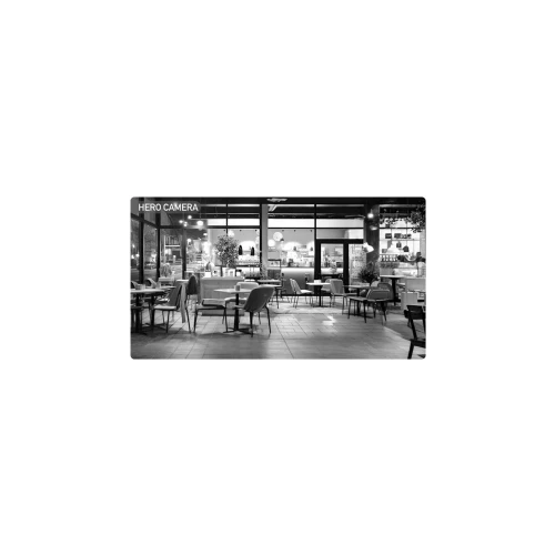 Czarno-białe zdjęcie przedstawia wnętrze kawiarni z pustymi stolikami i krzesłami, oświetlone delikatnym światłem. W tle widać ladę z ekspresami do kawy i dekoracje roślinne.