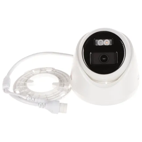 Na zdjęciu znajduje się biała kamera monitoringu z czarnym panelem przednim, obok której leży biały pierścień zaciskowy i kabel. Kamera ma dwa widoczne diody LED oraz obiektyw umieszczony centralnie.