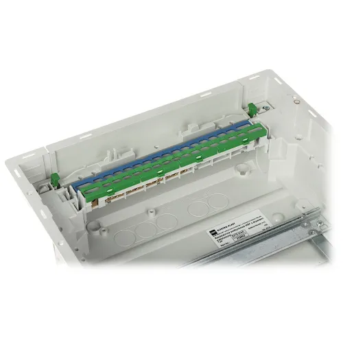 Zdjęcie przedstawia białą obudowę z zamontowaną listwą zaciskową w kolorze zielono-niebieskim. Wewnątrz obudowy widoczne są miejsca na przewody oraz metalowy wspornik.