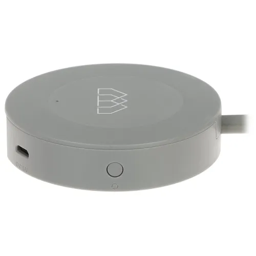 Szary, okrągły przycisk z logo na górze, posiada port micro USB i przycisk na boku. Urządzenie jest przeznaczone do włączania i wyłączania zasilania.