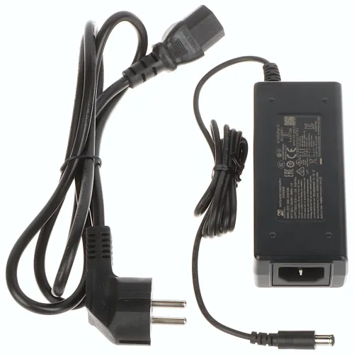 Na zdjęciu znajduje się czarny zasilacz z przewodem zasilającym oraz wtyczką. Zasilacz ma prostokątny kształt i widoczne są na nim oznaczenia techniczne.