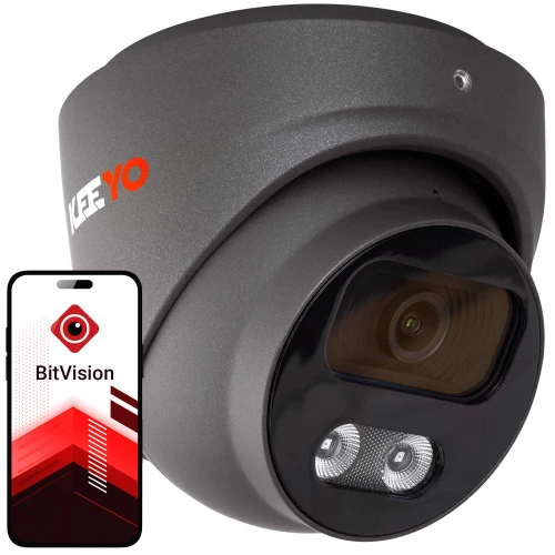 Na zdjęciu znajduje się czarna kamera monitoringu o nowoczesnym designie, obok której widoczny jest smartfon z aplikacją BitVision na ekranie. Kamera ma wyraźnie zaznaczone obiektyw i diody, a na obudowie widnieje logo producenta.