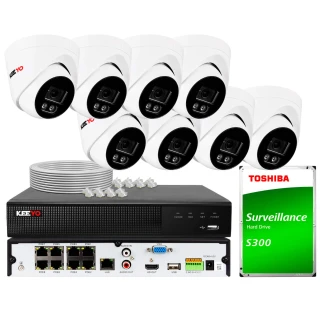 Na zdjęciu znajduje się zestaw do monitoringu, który obejmuje osiem białych kamer, rejestrator oraz dysk twardy Toshiba S300. W tle widoczne są również kable i złącza potrzebne do instalacji systemu.
